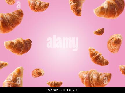 Viele frisch gebackene Croissants schweben oder fliegen. Croissants isoliert auf rosa Hintergrund. Levitation-Szene. Platz für Text kopieren. Werbung für Bäckerei, Konditorei. Kreatives Frühstück Stockfoto