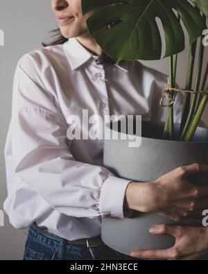 Die junge Frau steht mit einem großen Blumentopf mit Monstera Stockfoto