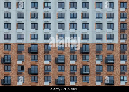 Fragment einer Wand eines mehrstöckigen weiß-braunen Gebäudes mit Fenstern und Balkonen. Stockfoto