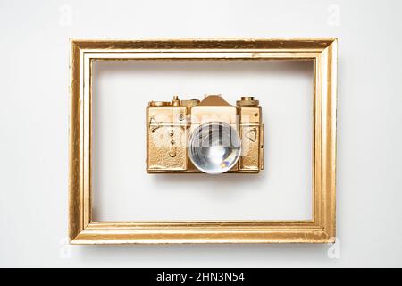 Goldene Kamera in goldenem Rahmen, mit einer Objektivkugel anstelle des Kameraobjektivs. Geringe Schärfentiefe Stockfoto