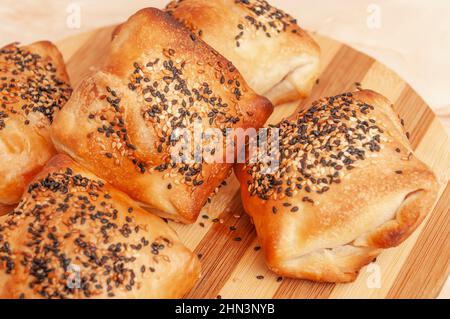 Mit Käse gefülltes Gebäck auf einem runden Holzteller, mit weißem und schwarzem Sesam Stockfoto