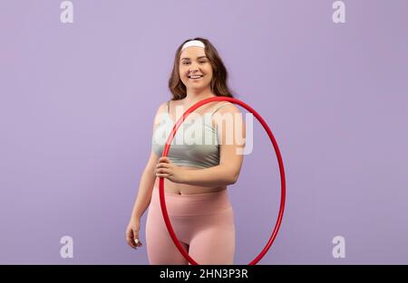 Fröhlich lächelnde Millennial european Plus size Athlet in Sportswear halten Hula Hoop Reifen bereit zum Training Stockfoto