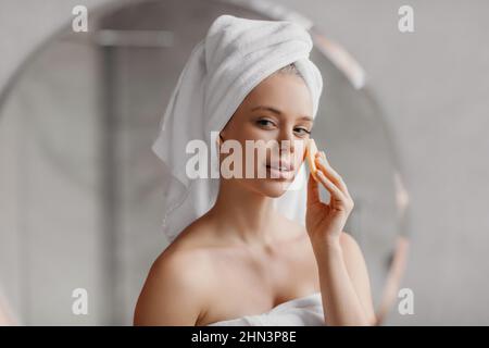 Hübsche Dame mit kosmetischen Schwamm genießen Gesichtshaut Routine, im Bad am Morgen stehen Stockfoto