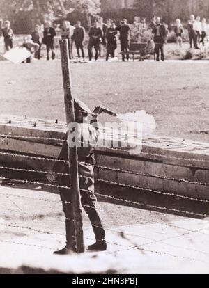 Vintage-Foto der Berliner Krise von 1961: Mauerbau. Kommunistischer "Volkspolizist", der zwischen Grenzzaun und Mauer steht, Stockfoto