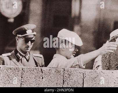 Vintage-Foto der Berliner Krise von 1961: Mauerbau. Ein Ost-Berliner Freimaurer, der von Einem kommunistischen Polizisten sorgfältig beobachtet wird, verdoppelt die Höhe der Stockfoto