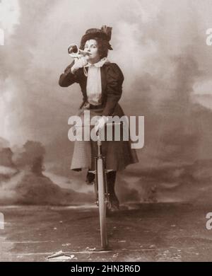 Vintage-Foto von Madge Lessing auf dem Fahrrad, das Musikhorn an den Lippen hält. 1898 Madge Lessing (1873 – 1966) war eine britische Bühnenschauspielerin und Sängerin, Pant Stockfoto