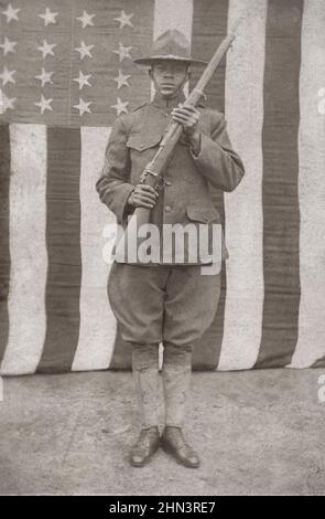 USA im Ersten Weltkrieg African American Soldier in Uniform und Feldhut mit Gewehr vor amerikanischer Flagge. 1917-1918 Stockfoto