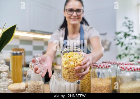 Frau, die ein Glas mit Cornflakes und Lebensmittelaufbewahrung in der Küche zeigt. Stockfoto