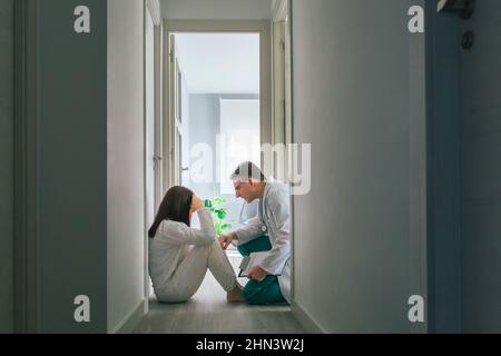 Arzt beruhigt mit Empathie eine Patientin, die auf dem Boden eines psychiatrischen Zentrums sitzt Stockfoto