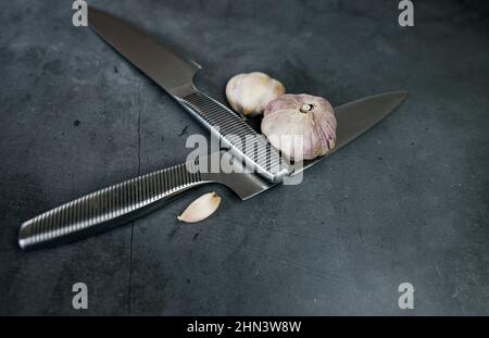 Knoblauchzwiebeln und Messer auf einem dunklen Steinbrett. Draufsicht. Stockfoto