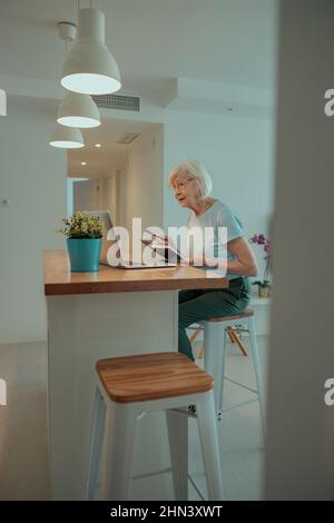 Ältere Frau, die zu Hause am Tisch sitzt Stockfoto