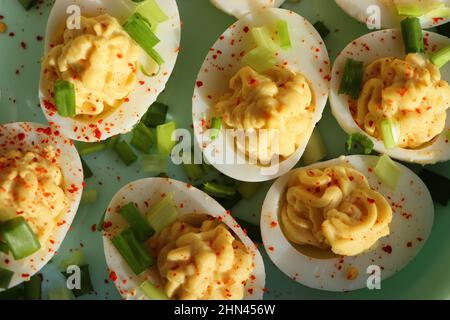 Deviled Eier bestreut mit Paprika und gehackte grüne Zwiebel auf einem grünen Teller auf einem Holztisch . Draufsicht Stockfoto