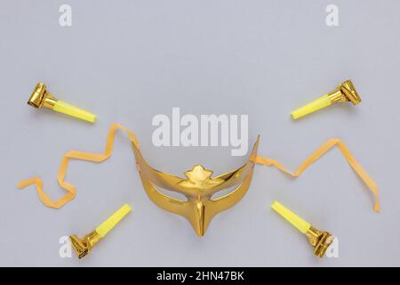 Goldene Karnevalsmaske auf festlichem Grau mit Party-Pfeifen Hintergrund. Karneval Saison, Feier, Kostüm Motto Party Konzept. Abstrakter minimalistischer Hintergrund. Draufsicht, Kopierbereich Stockfoto
