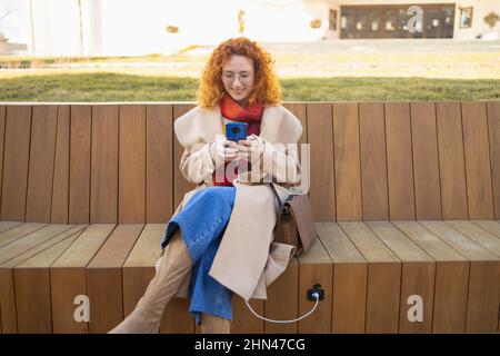 Junge Frau mit ihrem Smartphone auf einer intelligenten Bank in einer modernen Stadt Stockfoto