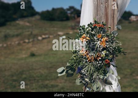 Florale dekorative Dekoration des weißen hölzernen Hochzeitsbogens mit frischen Blumen. Eine Farm halten, Boho Hochzeitszeremonie im Freien. Sommer Stockfoto