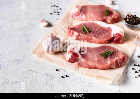 Ein Stück rohes frisches Schweinefleisch mit Rosmarin und Knoblauch auf einem vax-Papier auf weißem Hintergrund. Fleisch mit Gewürzen für Rezepte und Kochen. Stockfoto