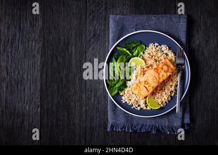 Portion pochierter Lachs in Kokosnusskalk-Sauce mit braunem Reis und frischem Spinat, Lachsfischcury mit Reis und Gemüse auf einem Teller, Blick von oben, Stockfoto