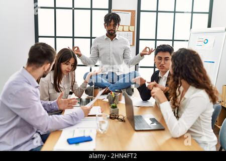 Geschäftsmann meditiert gern während des Meetings. Sitzen auf dem Schreibtisch in der Nähe streitenden Partnern im Büro. Stockfoto