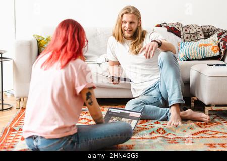Weißer Mann und Frau sprechen und lächeln, während sie zu Hause auf dem Boden sitzen Stockfoto