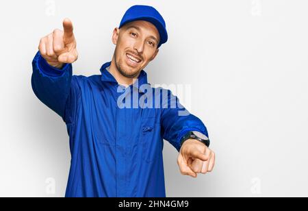 Glatze Mann mit Bart tragen Baumeister Jumpsuit Uniform zeigt auf Sie und die Kamera mit Fingern, lächelnd positiv und fröhlich Stockfoto