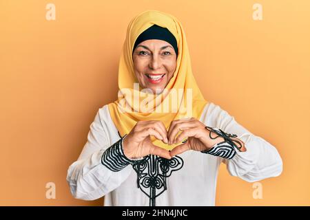 lateinamerikanische Frau mittleren Alters trägt traditionelle islamische Hijab Schal lächelnd in der Liebe tun Herz Symbol Form mit Händen. Romantisches Konzept. Stockfoto