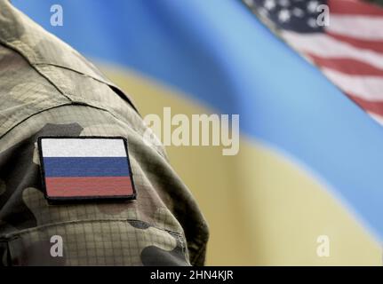 Flagge Russlands auf Militäruniform und Flaggen der Ukraine und der USA im Hintergrund. Russland gegen die Ukraine. Stockfoto