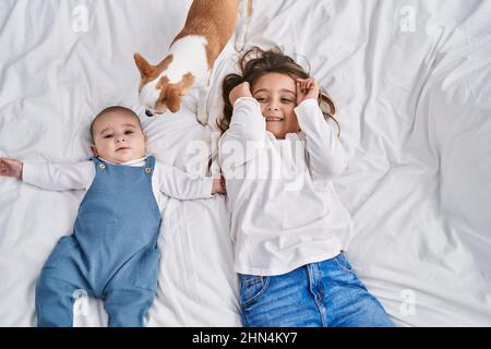 Bruder und Schwester lächeln selbstbewusst zusammen mit Hund auf dem Bett im Schlafzimmer liegen Stockfoto