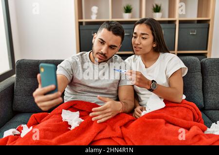 Junges lateinamerikanisches krankes Paar, das zu Hause eine medizinische Fernsultation mit dem Smartphone hat. Stockfoto