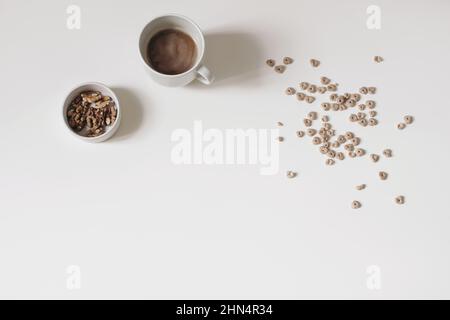 Das Frühstück ist still Life. Knuspriger Honig Hafer oder Buchweizen herzförmigen Getreide auf weißem Tischhintergrund isoliert. Tasse Kaffee, Schüssel mit Walnüssen. Gesund Stockfoto