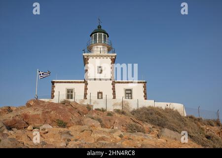 Der wunderschöne Leuchtturm Akrotiri auf der Insel Santorini Griechenland und die griechische Flagge daneben Stockfoto