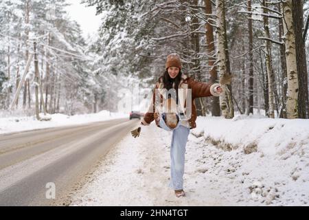 Fröhliche junge asiatische Frau, die in der Winternatur spazieren geht, Schnee in die Kamera tritt und lacht Stockfoto