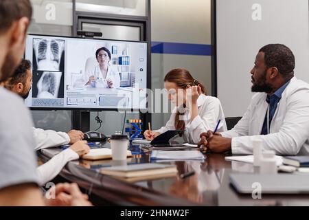 Junge Ärztin, die sich bei der Online-Präsentation der medizinischen Forschungsergebnisse bei einem digitalen Meeting Notizen unter Kollegen macht Stockfoto