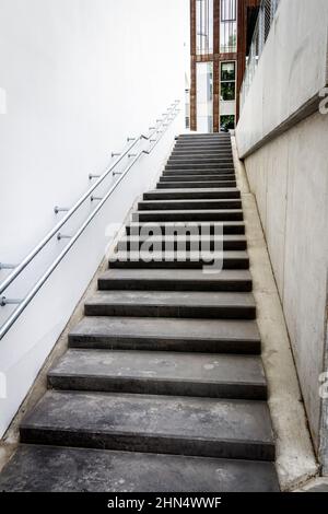 Leere Treppe, die mit einer Handschiene zwischen modernen Bürogebäuden hinauf führt. Stockfoto