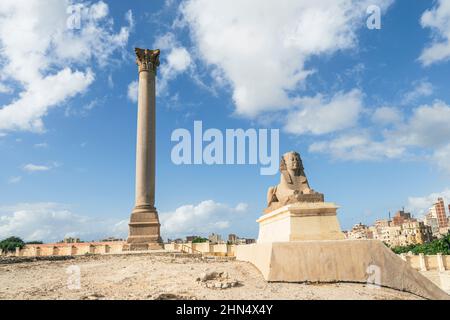 Der berühmte Pompeius-Pfeiler mit einer Sphinx in der oberägyptischen Stadt Alexandria. Ein beliebtes Reiseziel. Tag und blauer Himmel. Eine schöne Langzeitbelichtung Stockfoto