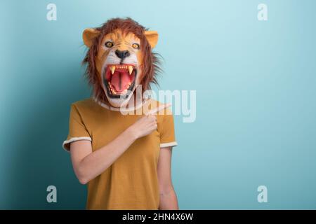 Frau in Löwenmaske, die mit Zeigefinger auf den leeren Raum zeigt, isoliert auf blauem Hintergrund Stockfoto