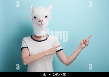 Frau in Alpaka-Maske, die mit Zeigefingern auf das leere Feld zeigt, isoliert auf blauem Hintergrund Stockfoto