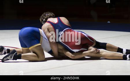 Nahaufnahme von zwei High School-Jungen, die während eines Wrestling-Matches unter einem Lichtfleck ringen. Stockfoto