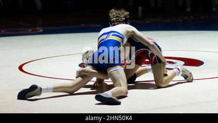 Zwei High School-Ringer ringen während eines Kampfes unter einem Lichtpunkt in einer dunklen Turnhalle. Stockfoto