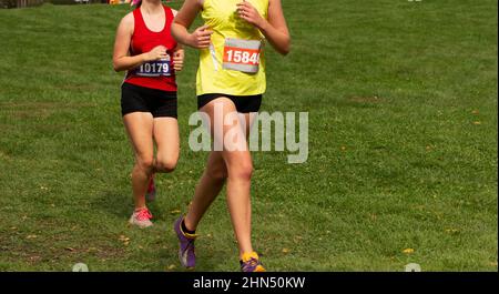 Zwei Mädchen der High School laufen 5K auf einem Grasfeld. Stockfoto