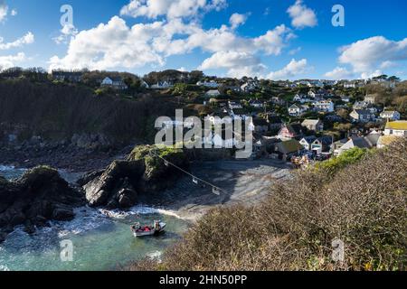 Blick auf Cadgwith Cove, Cornwall, zeigt die Häuser und ein Fischerboot, das sich dem Ufer nähert Stockfoto