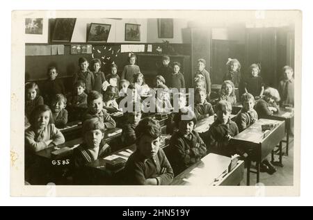 Originalpostkarte aus den frühen 1920er Jahren mit ernst aussehenden, gut erzogenen Jungen und Mädchen, die an Schreibtischen sitzen, die Arme gefaltet, in einem Klassenzimmer der Junior-Schule, Worthing, Sussex, England, Großbritannien Stockfoto