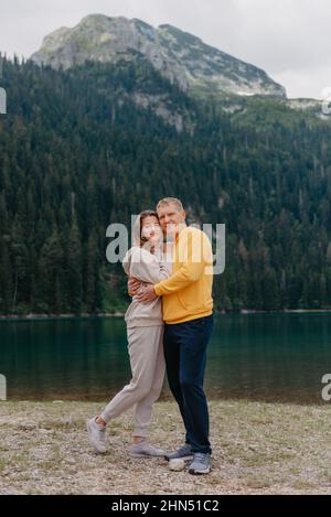 Romantisches Hochzeitspaar in Liebe am steinigen Ufer des Sees, malerische Aussicht auf die Berge. Die Braut und der Bräutigam. Schönes kaukasisches Paar umarmt Stockfoto