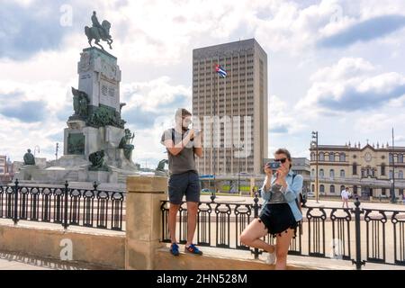 Ausländische Touristen machen Fotos am Antonio Maceo Park, wo man eine Skulptur sehen kann. Das Krankenhaus Hermanos Ameijeiras ist im Hintergrund zu sehen. Stockfoto