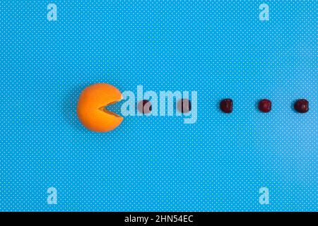 Kreatives Konkpet aus Orangen, die Kirschen fressen, auf lebhaftem blauen Hintergrund. Flacher Lay Pac man Stockfoto