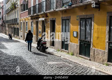 Sao Bento, Lissabon / Portugal - 12 28 2018: Junge Frau, die über die gepflasterten Straßen in den engen alten Straßen mit typischen bunten alten Häusern geht Stockfoto