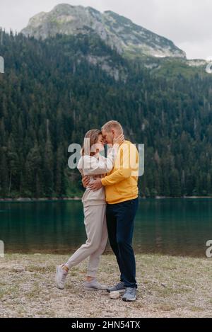 Romantisches Hochzeitspaar in Liebe am steinigen Ufer des Sees, malerische Aussicht auf die Berge. Die Braut und der Bräutigam. Schönes kaukasisches Paar umarmt Stockfoto
