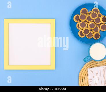 Frisch gebackene Plätzchen mit Schokolade und einer Tasse Tee für einen Snack auf hellblauem Hintergrund mit Papierkarton oder Kopierfläche. Flaches Dessertgericht Stockfoto