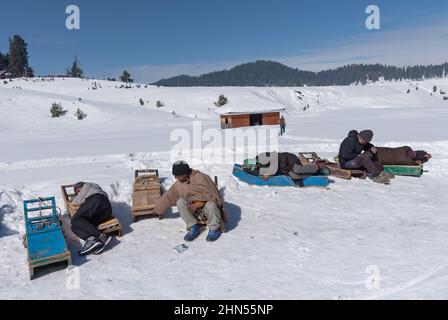 Baramulla, Indien. 12th. Februar 2022. Schlittenbesitzer ruhen sich auf ihren Schlitten aus, während sie an einem sonnigen Tag in Gulmarg auf Kunden warten. Gulmarg ist eine Stadt, eine Bergstation, ein beliebtes Skiziel und ein mitteiltes Gebietskomitee im Baramulla-Distrikt Jammu und Kaschmir. Die Stadt liegt in der Pir Panjal Range im westlichen Himalaya und liegt innerhalb der Grenzen des Gulmarg Wildlife Sanctuary. Kredit: SOPA Images Limited/Alamy Live Nachrichten Stockfoto