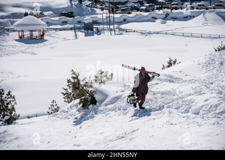 Baramulla, Indien. 12th. Februar 2022. Ein alter Mann geht an einem sonnigen Tag in Gulmarg an einem Hang entlang. Gulmarg ist eine Stadt, eine Bergstation, ein beliebtes Skiziel und ein mitteiltes Gebietskomitee im Baramulla-Distrikt Jammu und Kaschmir. Die Stadt liegt in der Pir Panjal Range im westlichen Himalaya und liegt innerhalb der Grenzen des Gulmarg Wildlife Sanctuary. Kredit: SOPA Images Limited/Alamy Live Nachrichten Stockfoto
