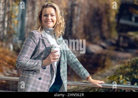 Porträt einer attraktiven lächelnden Frau mittleren Alters in karierter Jacke und grauem Rollkragen-Pullover stehen auf Metallbrücke. Stockfoto